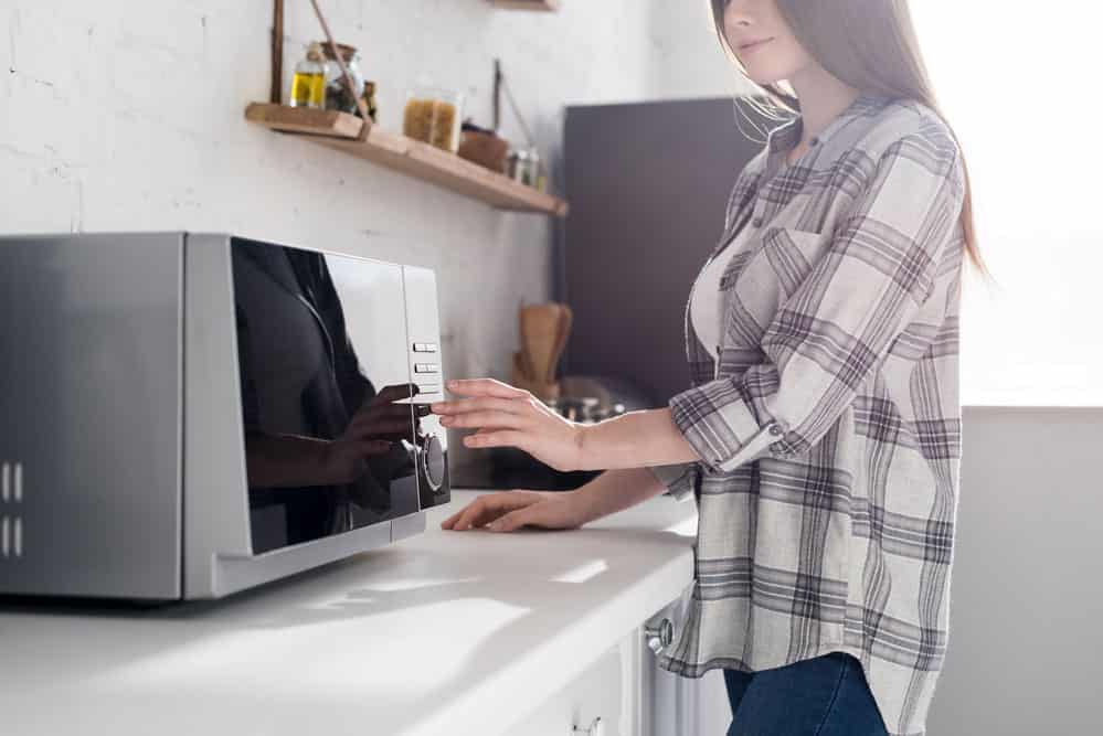 Woman in a shirt using a microwave in the kitchen